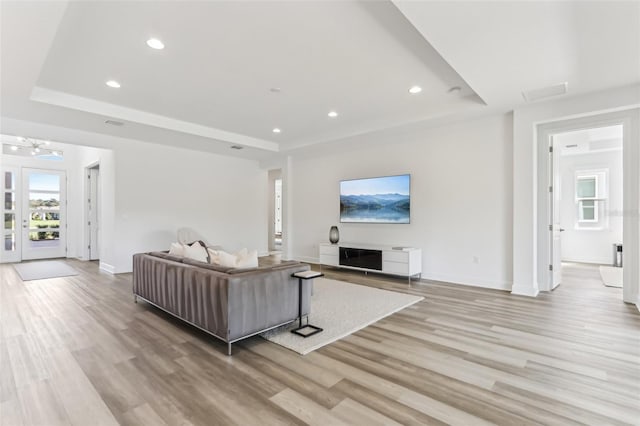 living area featuring light wood-style floors, a tray ceiling, and recessed lighting