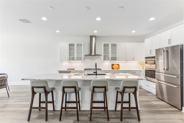 kitchen featuring white cabinetry, a kitchen breakfast bar, appliances with stainless steel finishes, wall chimney exhaust hood, and a center island with sink