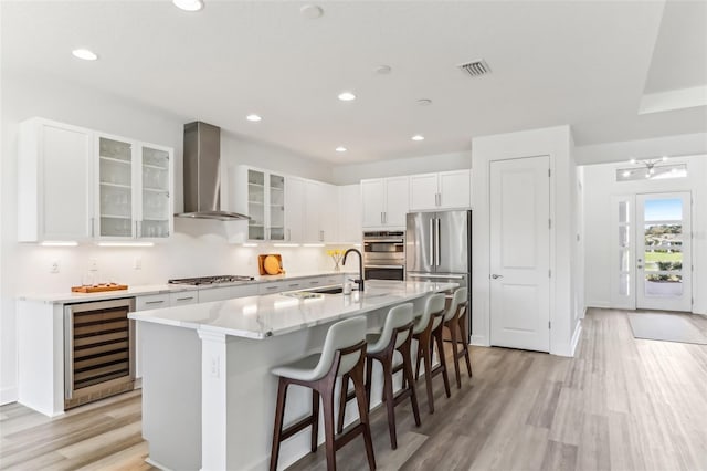 kitchen featuring wine cooler, stainless steel appliances, visible vents, wall chimney range hood, and a kitchen breakfast bar