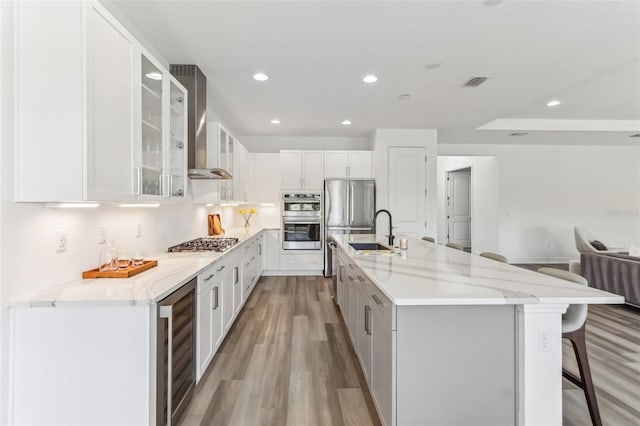 kitchen with beverage cooler, a sink, visible vents, appliances with stainless steel finishes, and wall chimney exhaust hood