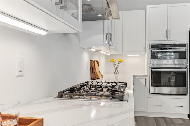 kitchen with appliances with stainless steel finishes, dark wood finished floors, light stone countertops, and white cabinets