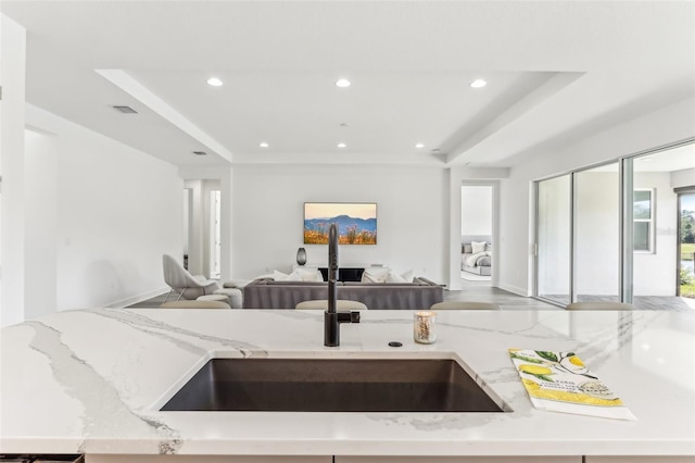 kitchen with recessed lighting, a raised ceiling, open floor plan, and light stone countertops