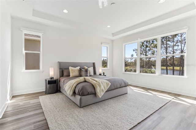 bedroom featuring light wood finished floors, a tray ceiling, recessed lighting, and baseboards