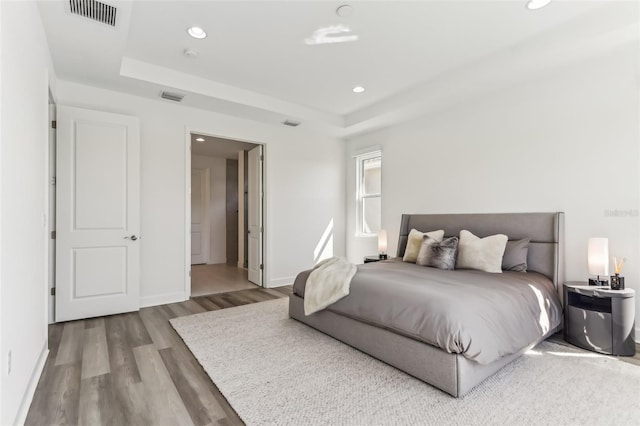 bedroom featuring baseboards, visible vents, wood finished floors, a tray ceiling, and recessed lighting