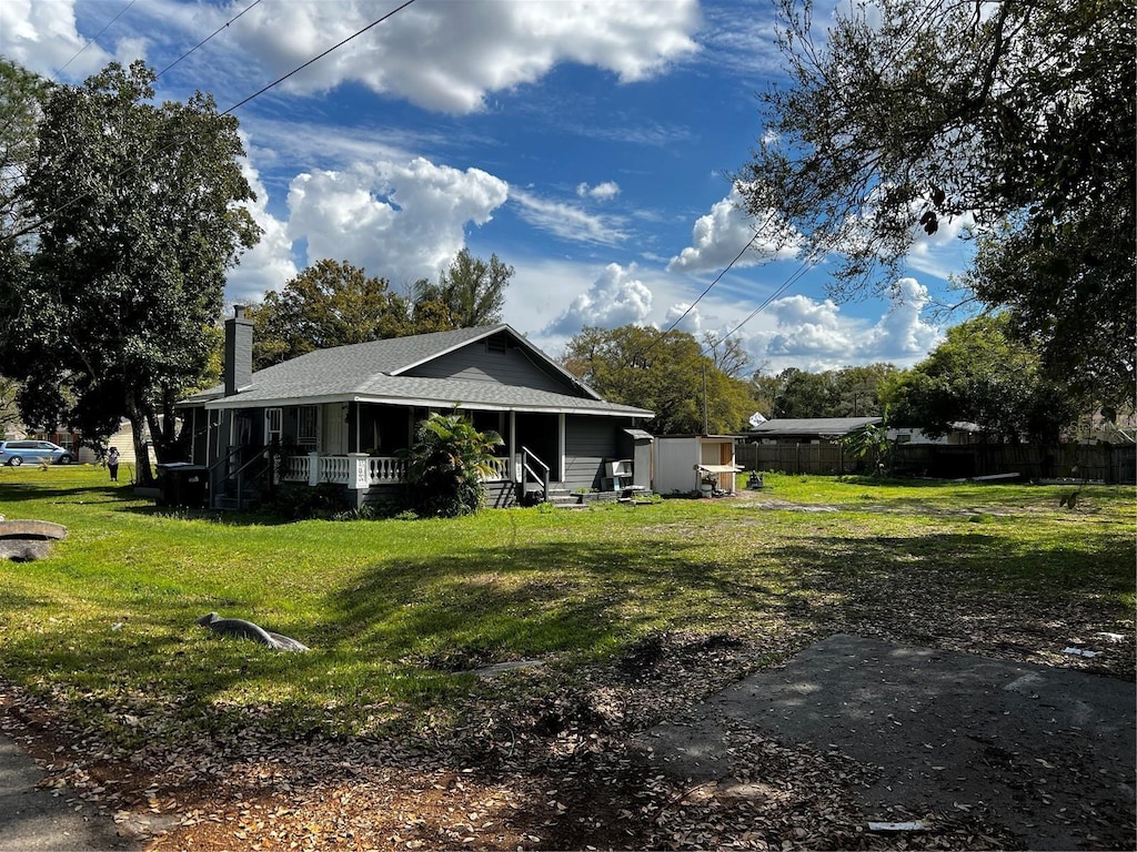 exterior space with a shingled roof, a lawn, a chimney, covered porch, and fence