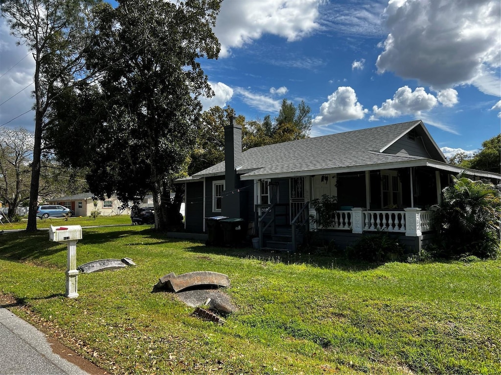 view of front facade with a porch, a shingled roof, a chimney, and a front lawn