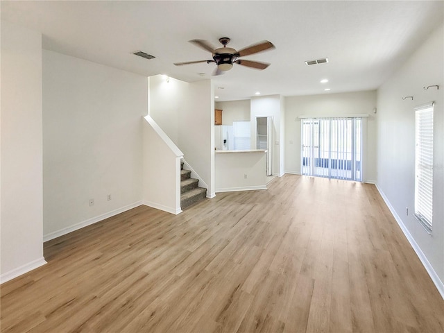 unfurnished living room with light wood-style floors, visible vents, stairway, and baseboards