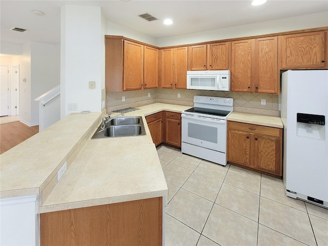 kitchen with a peninsula, white appliances, visible vents, and a sink