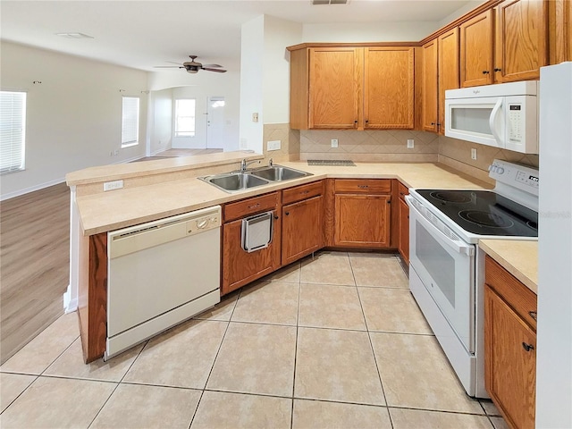 kitchen featuring light tile patterned floors, backsplash, a sink, white appliances, and a peninsula