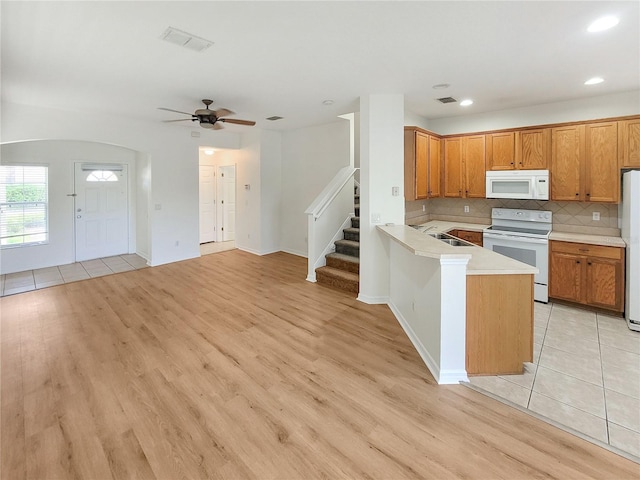 kitchen featuring light countertops, decorative backsplash, a sink, white appliances, and a peninsula