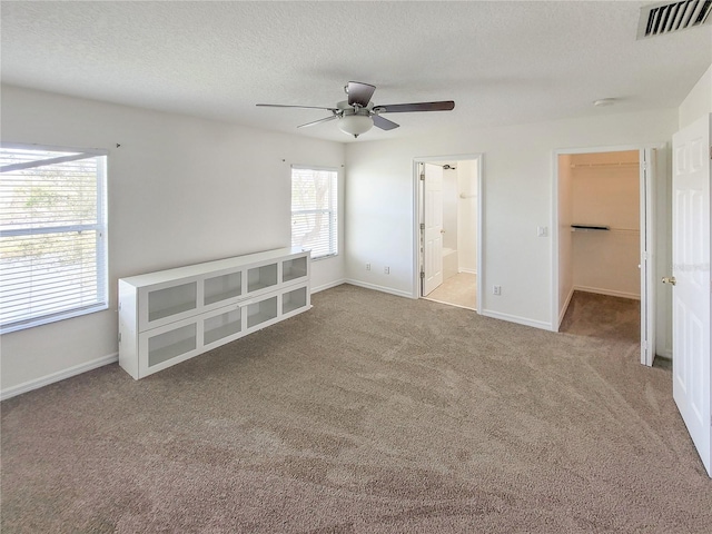 unfurnished bedroom featuring carpet, visible vents, a spacious closet, a textured ceiling, and baseboards