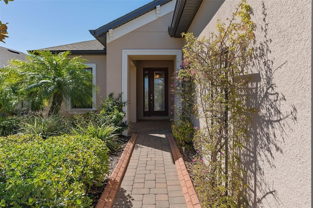 view of exterior entry featuring roof with shingles and stucco siding