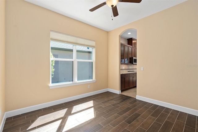 unfurnished room featuring baseboards, arched walkways, a ceiling fan, and wood finish floors