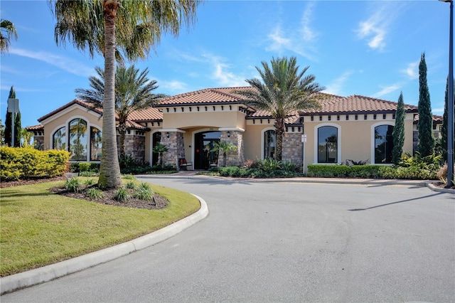 mediterranean / spanish-style home featuring stone siding, a tiled roof, a front lawn, and stucco siding