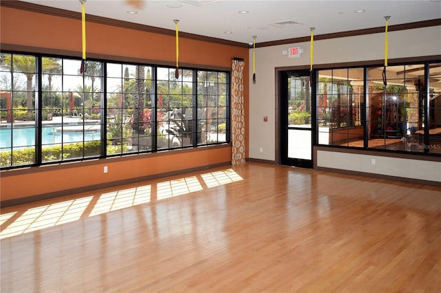 unfurnished room featuring baseboards, plenty of natural light, wood finished floors, and crown molding