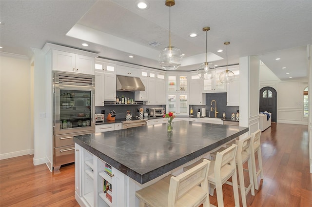 kitchen with a tray ceiling, open shelves, tasteful backsplash, oven, and under cabinet range hood