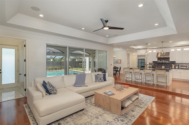 living room featuring ceiling fan, light wood finished floors, a raised ceiling, and a toaster