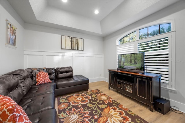 living area with a wainscoted wall, a raised ceiling, a decorative wall, and light wood-type flooring