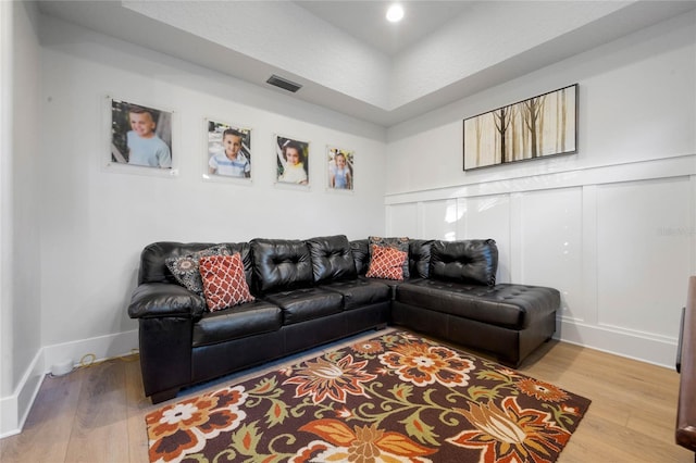 living area with visible vents, a decorative wall, baseboards, and wood finished floors