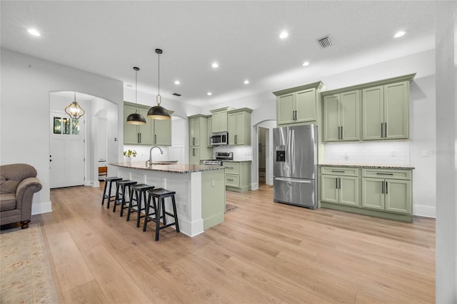 kitchen with a breakfast bar, a sink, stainless steel appliances, arched walkways, and green cabinetry