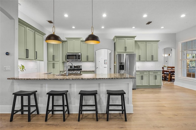 kitchen featuring arched walkways, stainless steel appliances, and green cabinets