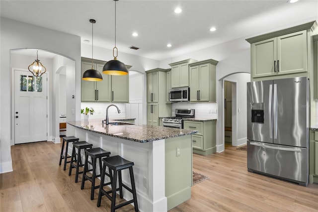 kitchen featuring green cabinets, a sink, arched walkways, and stainless steel appliances