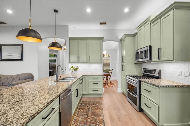 kitchen featuring light wood finished floors, green cabinets, light stone countertops, stainless steel appliances, and a sink