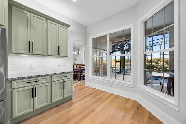 kitchen with light stone counters, green cabinetry, light wood-style flooring, arched walkways, and decorative backsplash