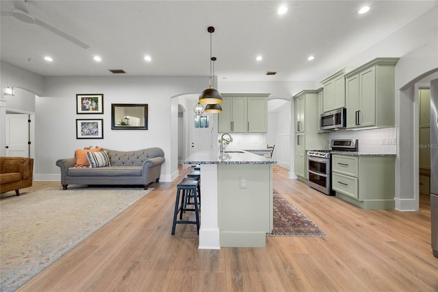 kitchen with green cabinetry, a kitchen breakfast bar, arched walkways, and appliances with stainless steel finishes