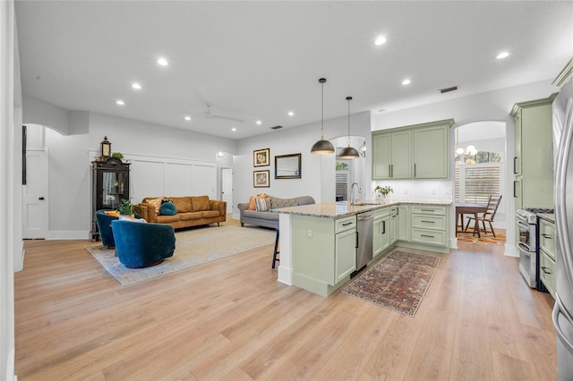 kitchen featuring a breakfast bar, a sink, stainless steel appliances, arched walkways, and green cabinets