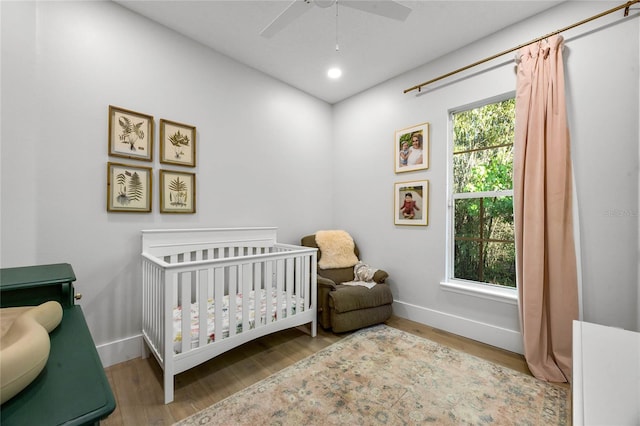 bedroom with a crib, wood finished floors, baseboards, and a ceiling fan