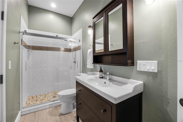 bathroom featuring vanity, a shower stall, toilet, and a textured wall