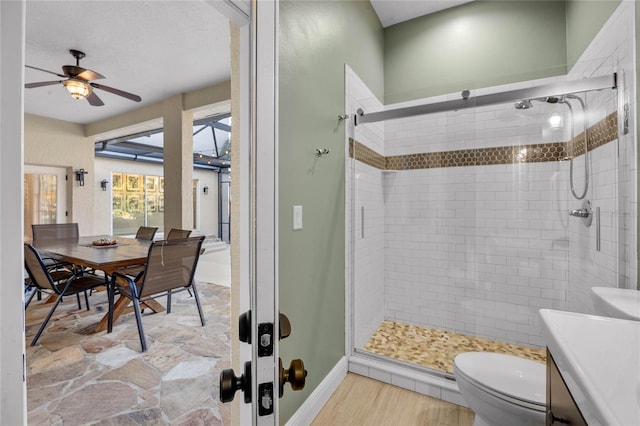 bathroom with toilet, a shower stall, baseboards, ceiling fan, and vanity