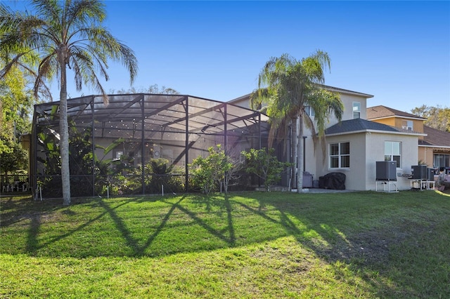 rear view of property featuring a lanai, a yard, central AC, and stucco siding