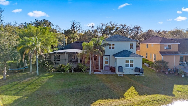 back of property with a trampoline, a yard, and stucco siding