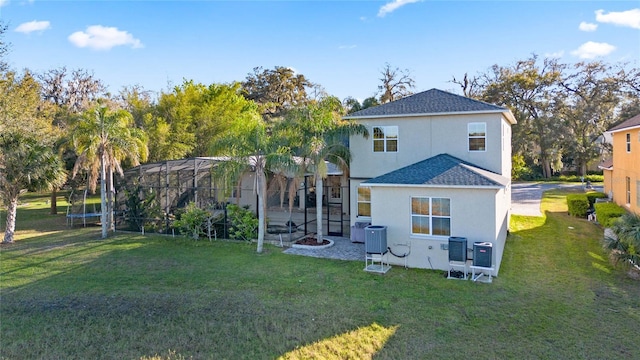 rear view of house featuring a trampoline, a lanai, roof with shingles, stucco siding, and a yard