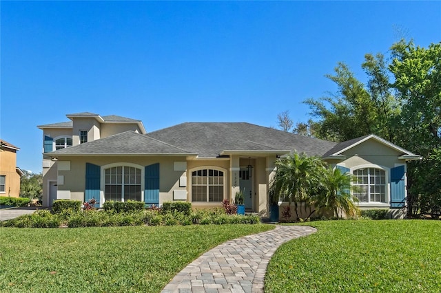 view of front of property with stucco siding, a front lawn, and roof with shingles