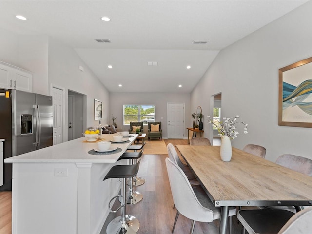 kitchen featuring visible vents, light wood-style flooring, a center island, vaulted ceiling, and white cabinetry