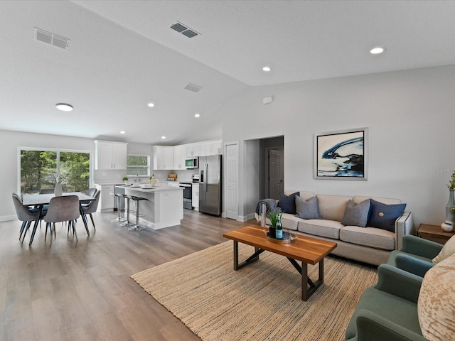 living area featuring baseboards, visible vents, vaulted ceiling, and wood finished floors