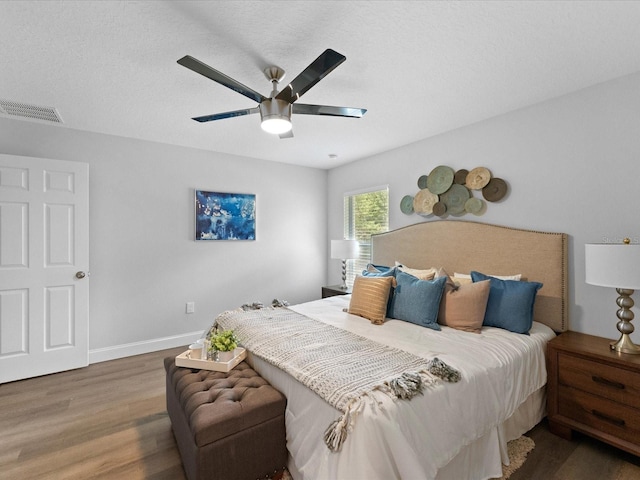 bedroom featuring ceiling fan, a textured ceiling, wood finished floors, visible vents, and baseboards