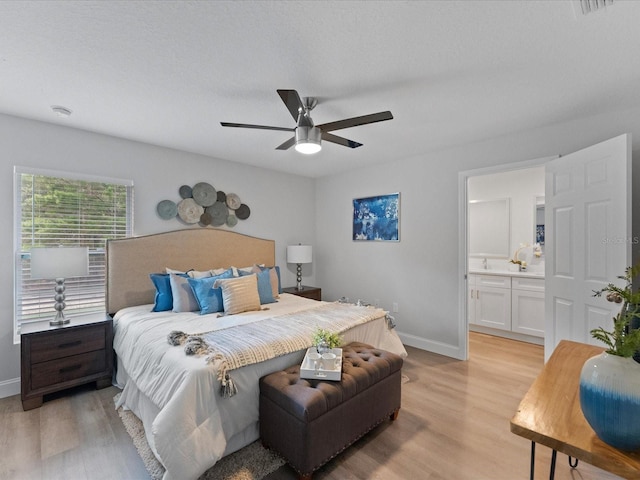 bedroom featuring ensuite bathroom, light wood finished floors, a ceiling fan, and baseboards