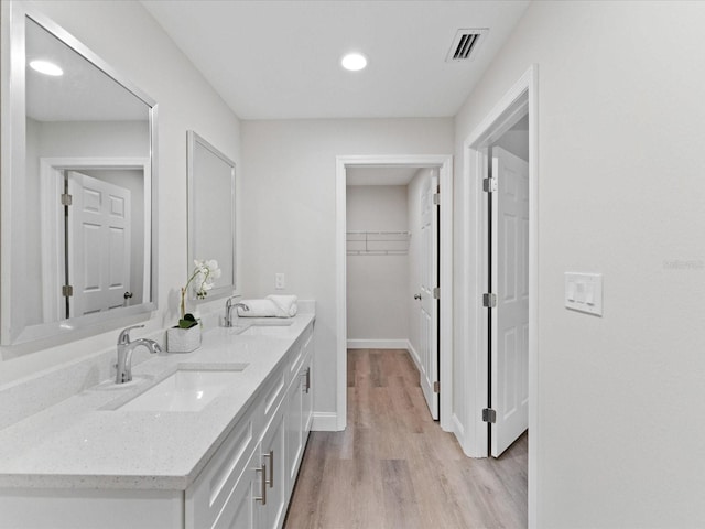 bathroom with double vanity, wood finished floors, a sink, and visible vents