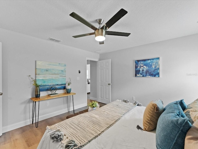 bedroom featuring baseboards, a textured ceiling, visible vents, and wood finished floors