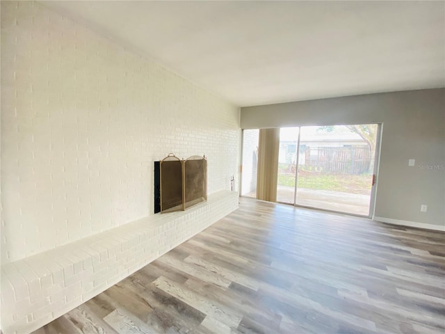 unfurnished living room featuring brick wall, a brick fireplace, wood finished floors, and baseboards