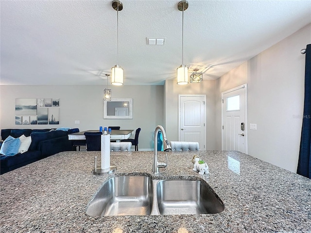 kitchen featuring pendant lighting, visible vents, a sink, a textured ceiling, and dark stone counters