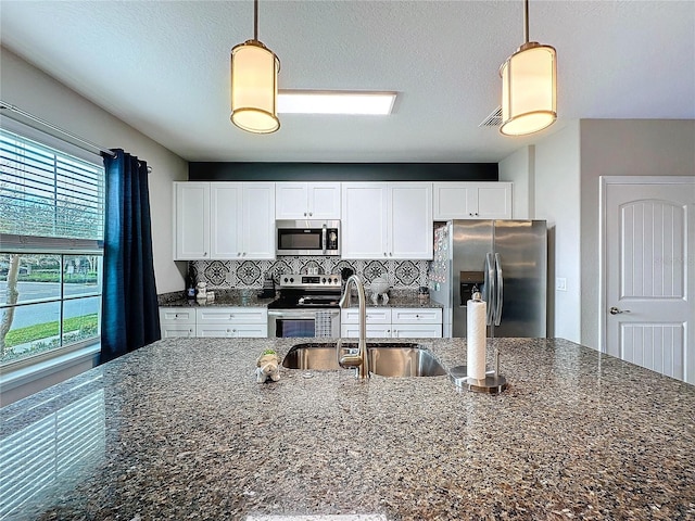 kitchen with stainless steel appliances, white cabinetry, hanging light fixtures, and decorative backsplash