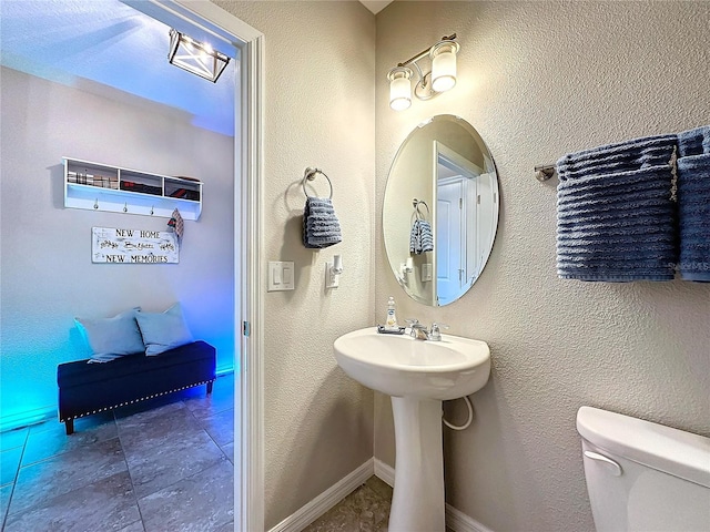 bathroom with baseboards, a textured wall, and toilet