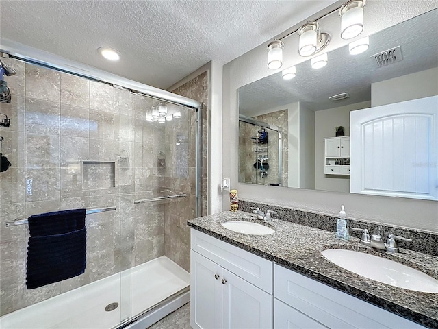 full bathroom with a stall shower, a textured ceiling, visible vents, and a sink