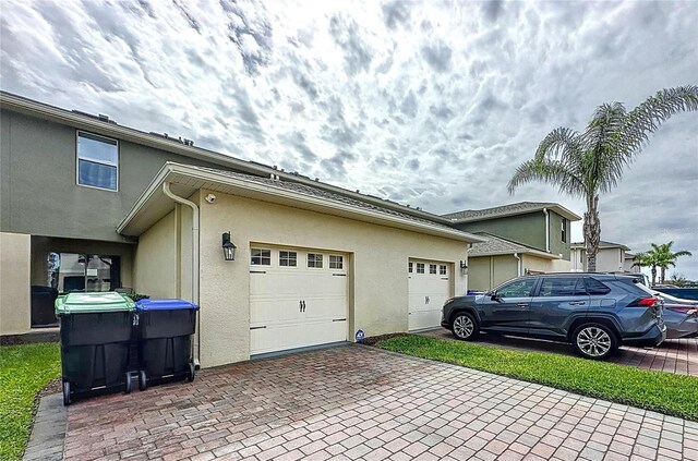 view of side of property featuring a garage, decorative driveway, and stucco siding