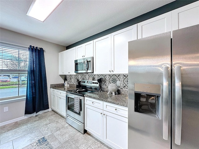 kitchen with stainless steel appliances, decorative backsplash, white cabinets, dark stone countertops, and baseboards